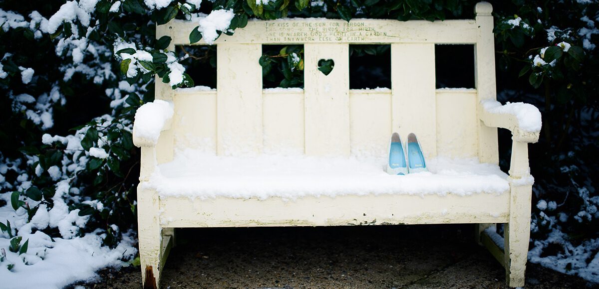The bride’s wedding shoes sit on a white bench surrounded by snow covered trees