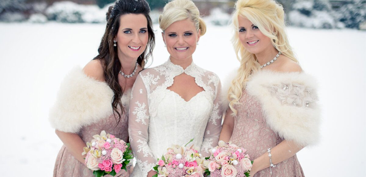 The bride and her two bridesmaids are dressed beautifully for a winter wedding wearing white boleros