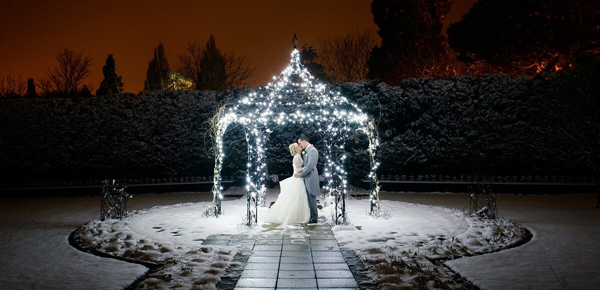 The happy newlyweds steal a kiss under the romantically lit iron Pavilion in the Walled Garden