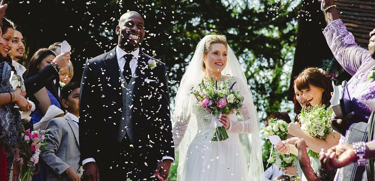 Wedding guests throw confetti over bride and groom
