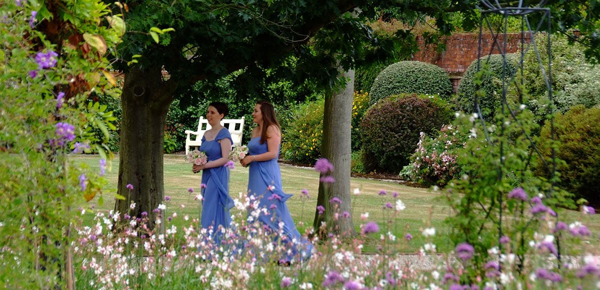 Bridesmaids in blue dresses walking down the Long Walk at Gaynes Park.