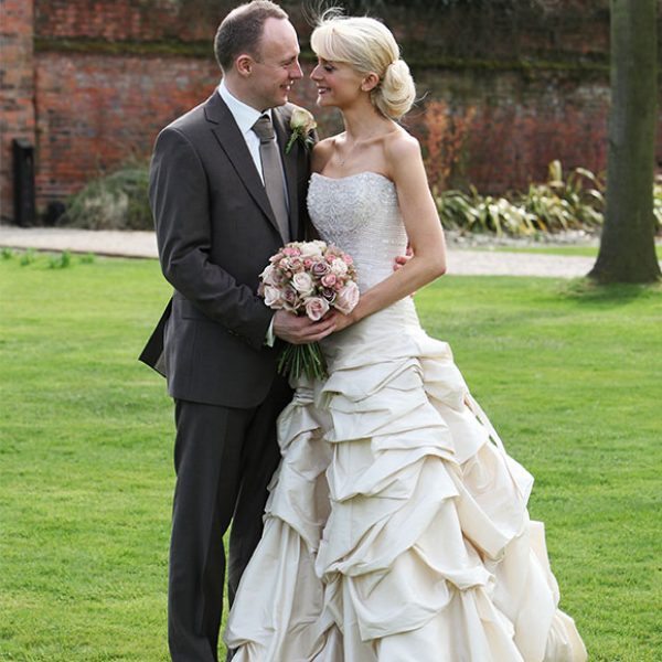 Bride with ruffled wedding dress and groom in gardens of their wedding venue in Essex