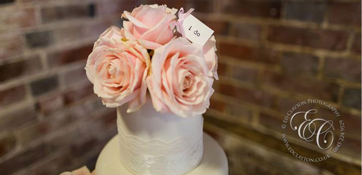 Pretty ivory wedding cake with pink roses at a barn wedding reception in Essex