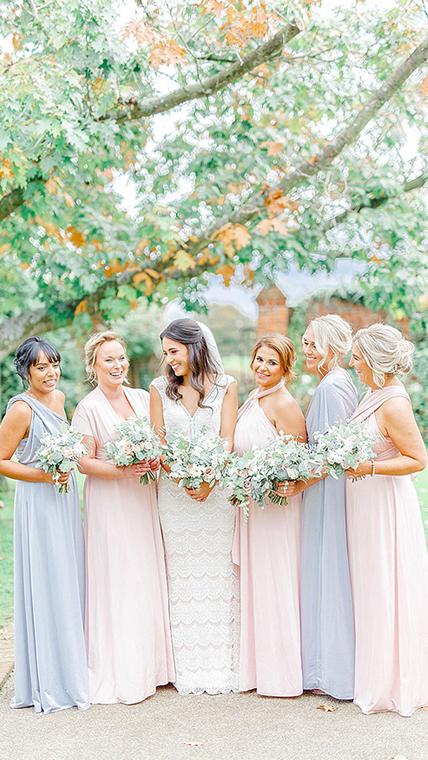 A bride smiles with her bridesmaids dressed in pale blue and pink bridesmaid dresses - wedding ideas