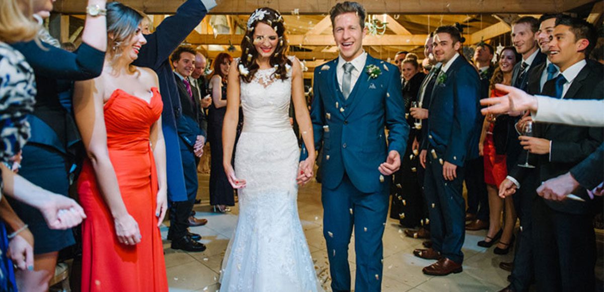 Bride and groom during a confetti throw with wedding guests – barn weddings Essex.