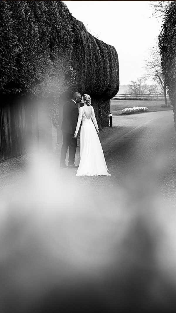 A bride and groom kiss as they walk along the wedding entrance drive of the countryside wedding venue