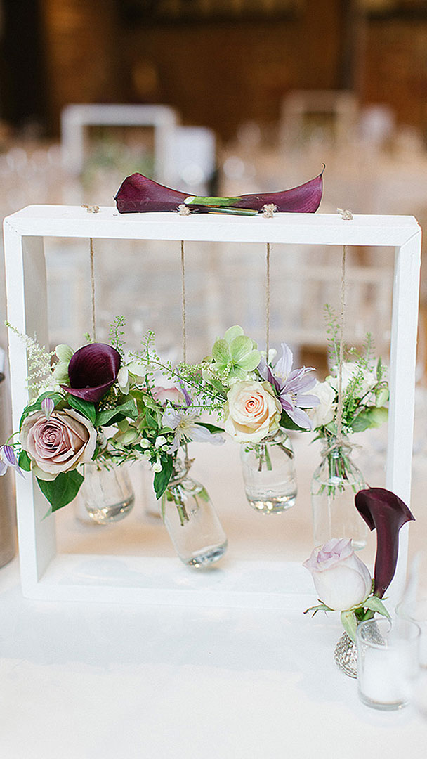 Pink and purple flowers hang in small glass jars as table centrepieces at this pretty summer wedding