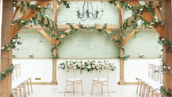 Ivy entwined with white roses is wrapped around the exposed oak beams inside the wedding ceremony Orangery