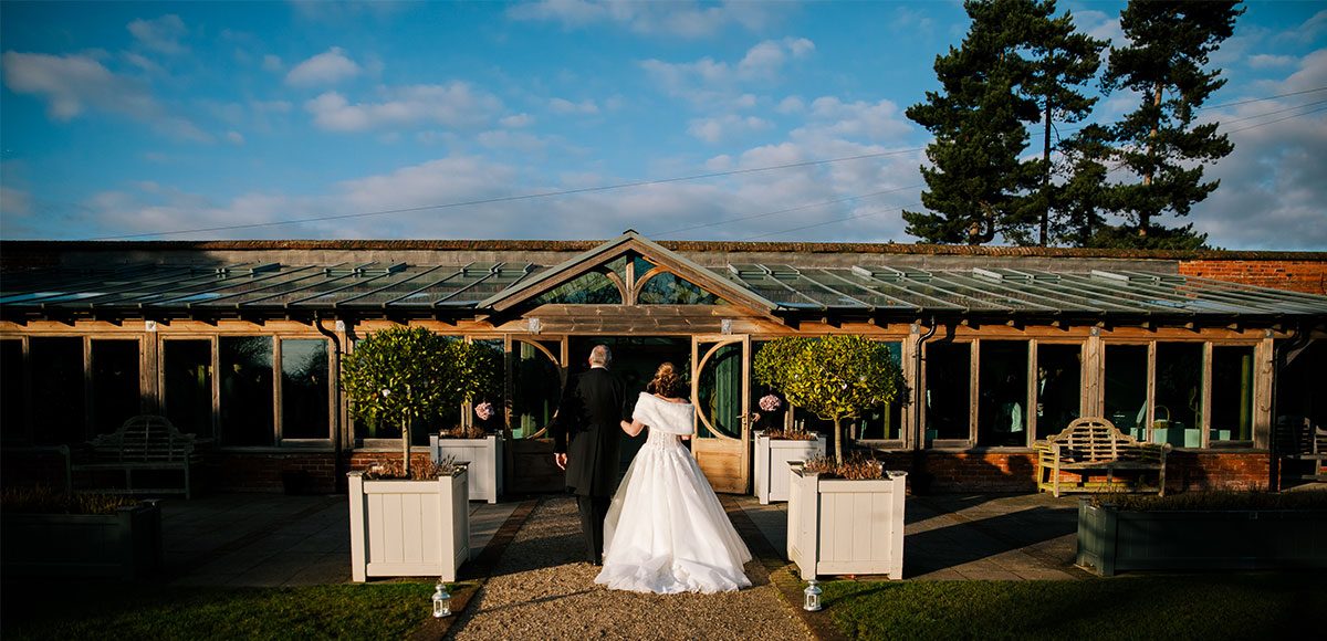 Bride walking down the Long Walk to the aisle inside of the Orangery – venue hire Essex.