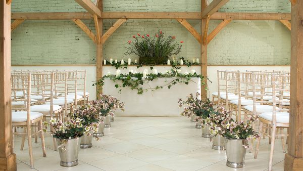 Beautiful pink flowers in silver planters line the wedding aisle at this stunning wedding ceremony barn
