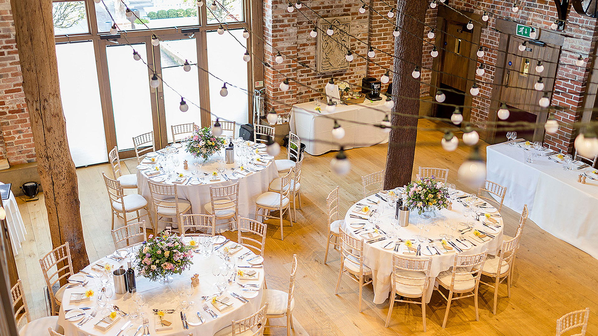 The Mill Barn is set up for a wedding with beautiful yellow and pink flowers for the table centrepieces