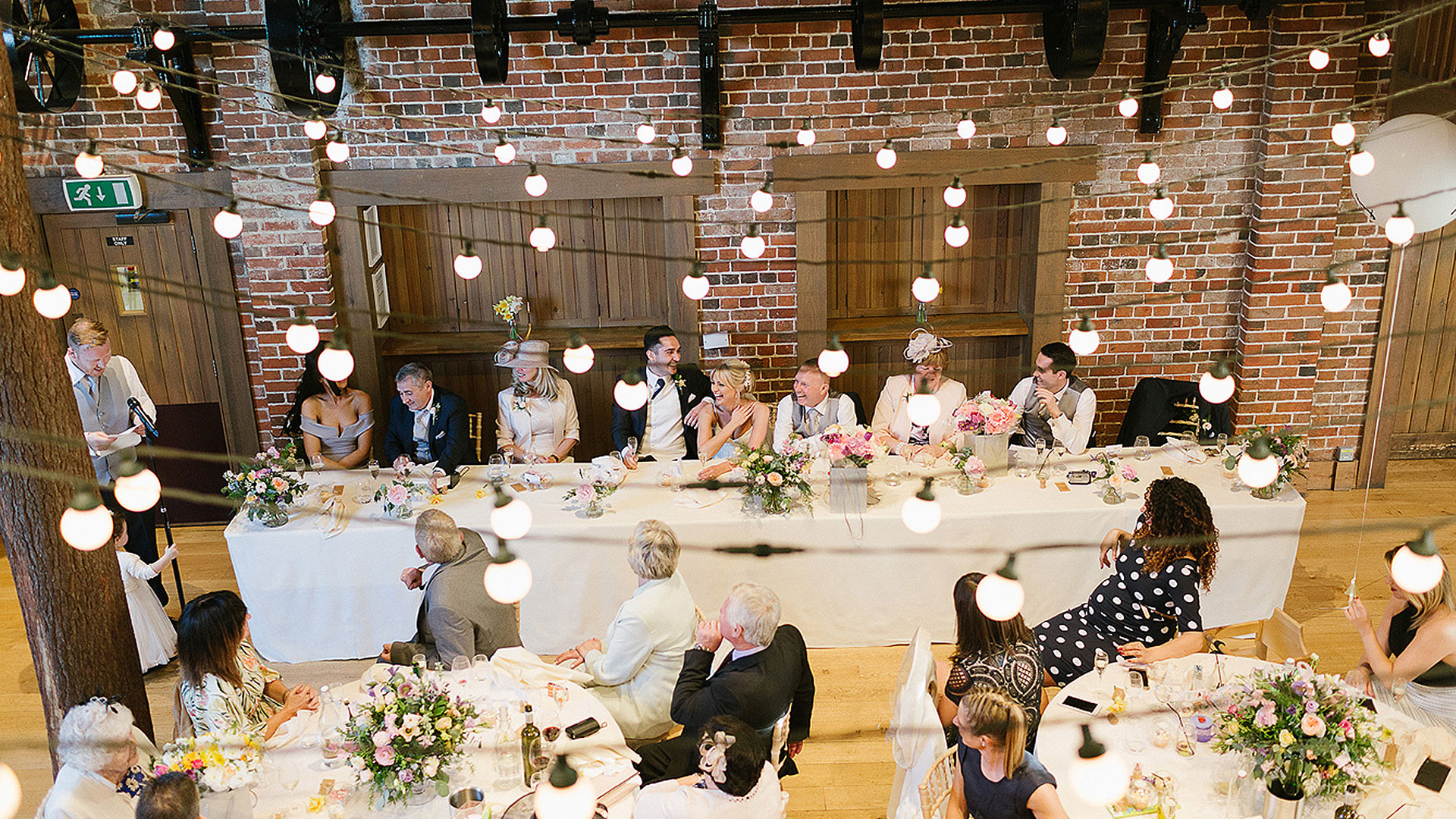 A wedding party enjoy the wedding speeches inside the stunning Mill Barn with exposed oak beams