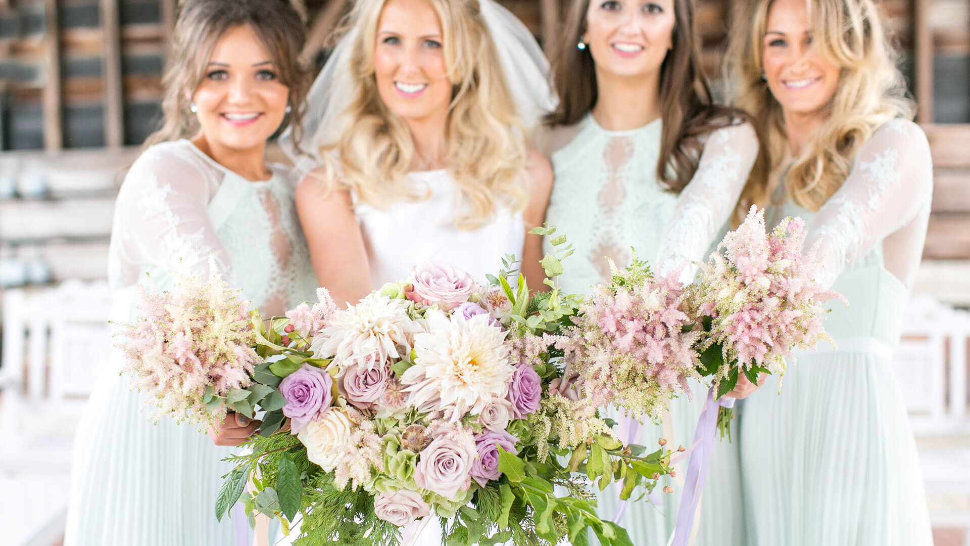 A bride and her bridesmaids stand in the Gather Barn holding their pale purple flowers - wedding ideas