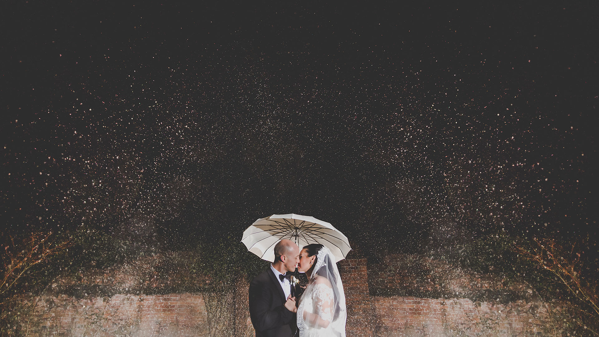 A couple kiss under falling snow at Gaynes Park winter wedding venue in Essex