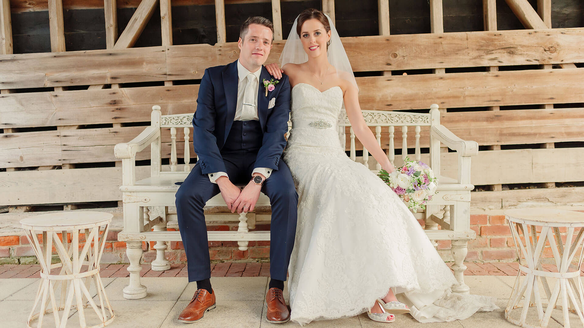 A bride and groom steal a moment on a white wedding bench - barn weddings Essex