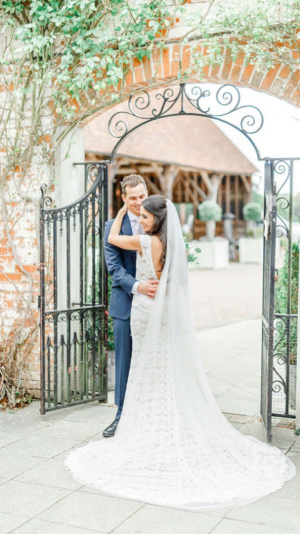 A happy couple embrace as they stand by an iron gate leading to the Gather Barn - Essex wedding venues