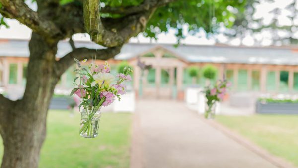 Flowers hang from glass jars in the Walled Garden for a summer wedding - summer wedding ideas