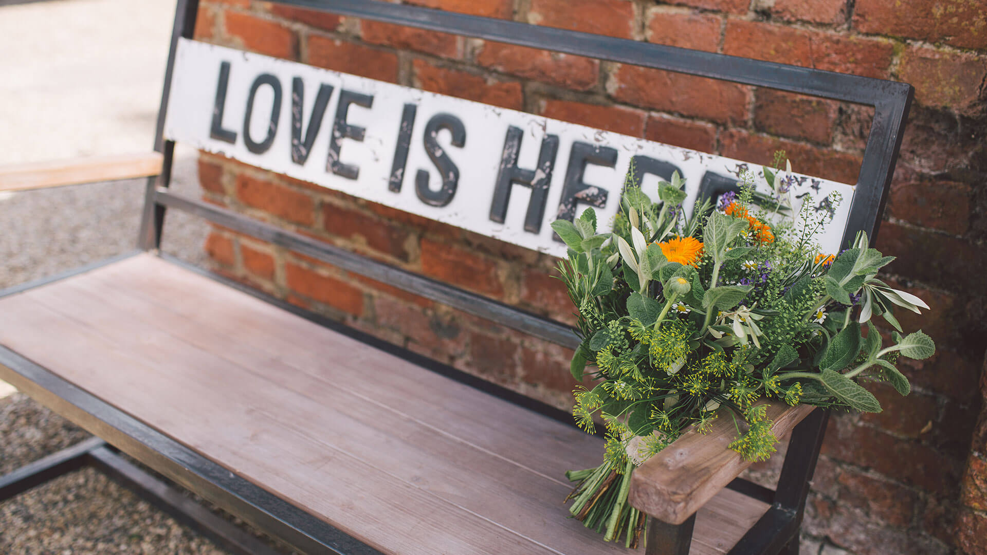 Pretty summer wedding flowers or green and yellow are placed on a bench that reads love is here