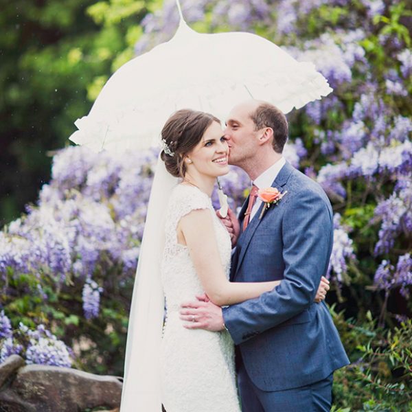 A groom kisses his bride under a white vintage wedding parasol – spring wedding ideas