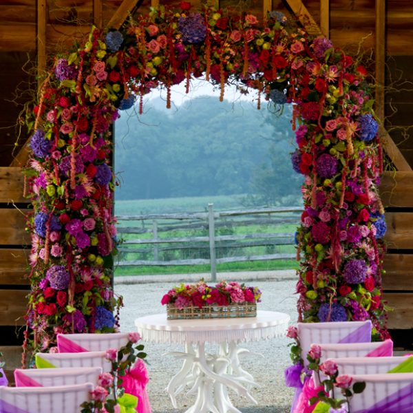 Colour is brought into this outside wedding ceremony with chairs dressed in bright pink and purple chair sashes