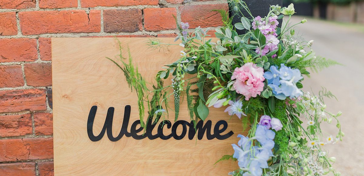 A wooden Welcome sign is decorated with wild flowers for a spring wedding