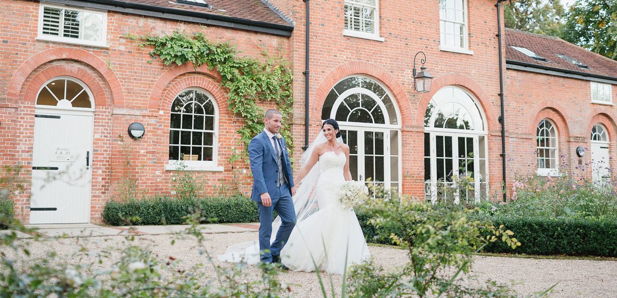 The bride and groom show their happiness as they walk in the gardens in front of the Coach House at Gaynes Park