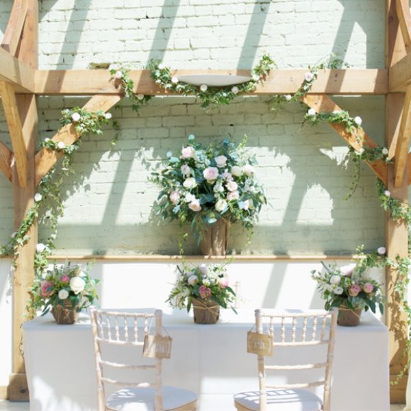 Chairs and beams are decorated with pastel flowers ready for a romantic wedding ceremony in the Orangery at Gaynes Park