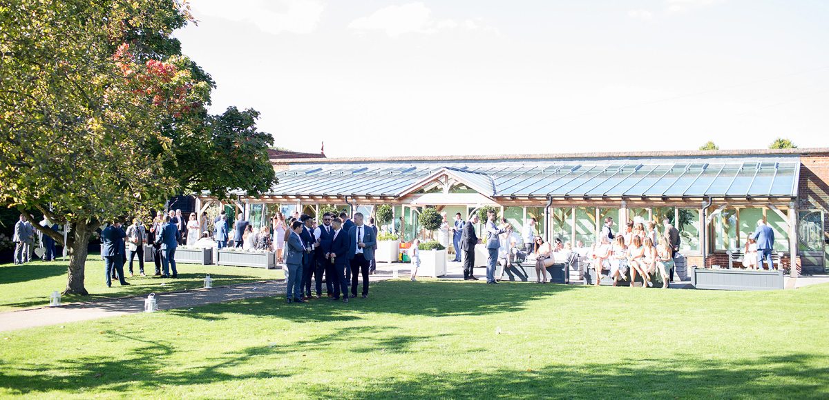 Guests enjoy wedding reception drinks outside the Orangery in the Walled Gardens at Gaynes Park
