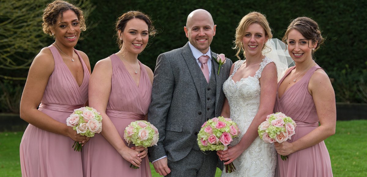 The bridesmaids wear blush pink as they stand with the bride and groom at the Essex wedding venue