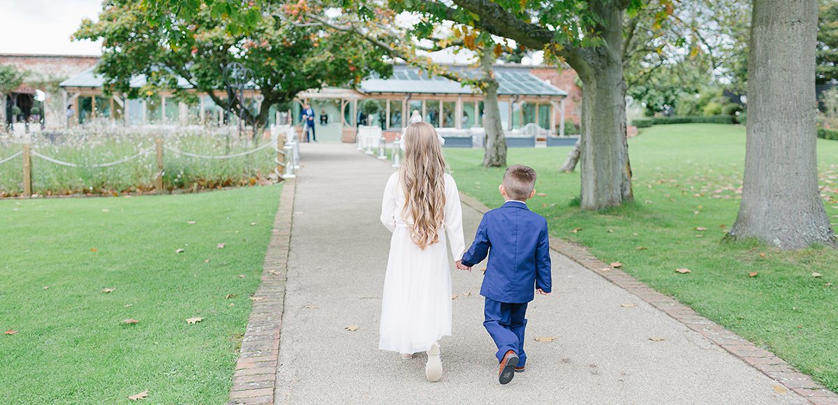 The flower girl and page boy walk hand down the Long Walk towards the wedding ceremony at Gaynes Park