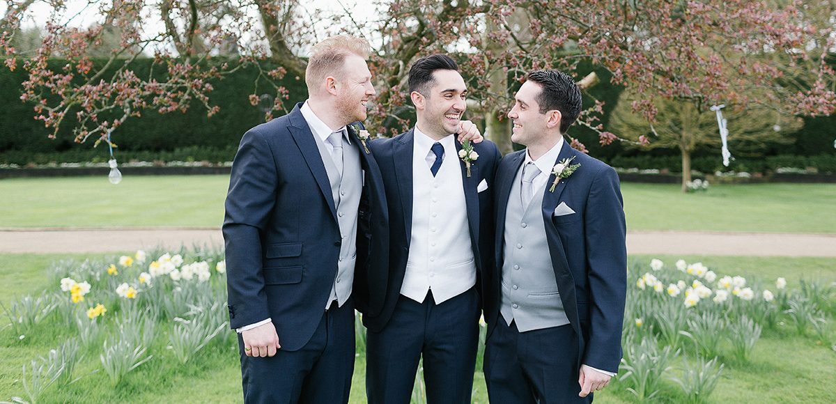 The groom and his groomsmen stand among the daffodils in the gardens at Gaynes Park in Essex