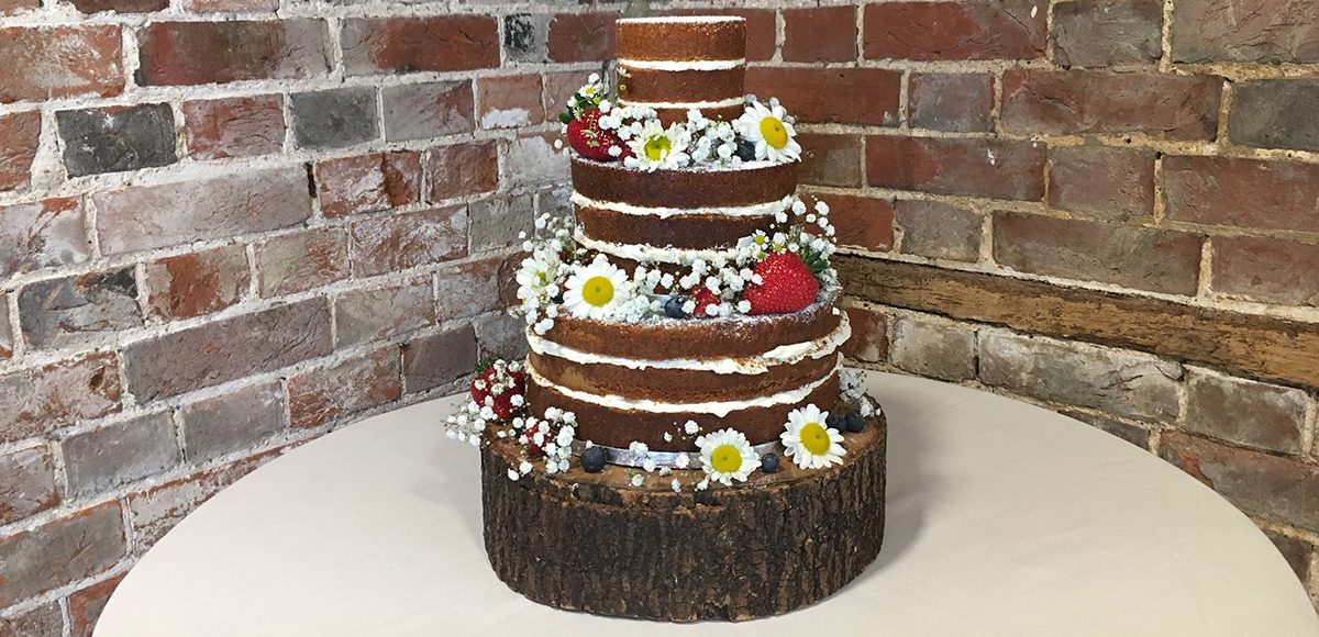 This naked wedding cake adorned with daisies and berries is perfect for a rustic wedding