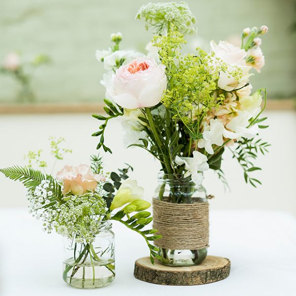 Jam jars wrapped in hessian and filled with wedding flowers create a rustic wedding look