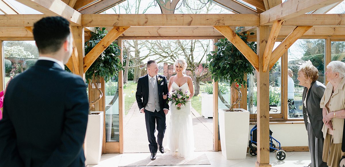 The bride and her father enter the wedding ceremony in the Orangery at Gaynes Park