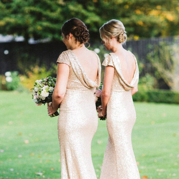 The bridesmaids wear gold dresses as they walk down the aisle towards the Orangery at Gaynes Park