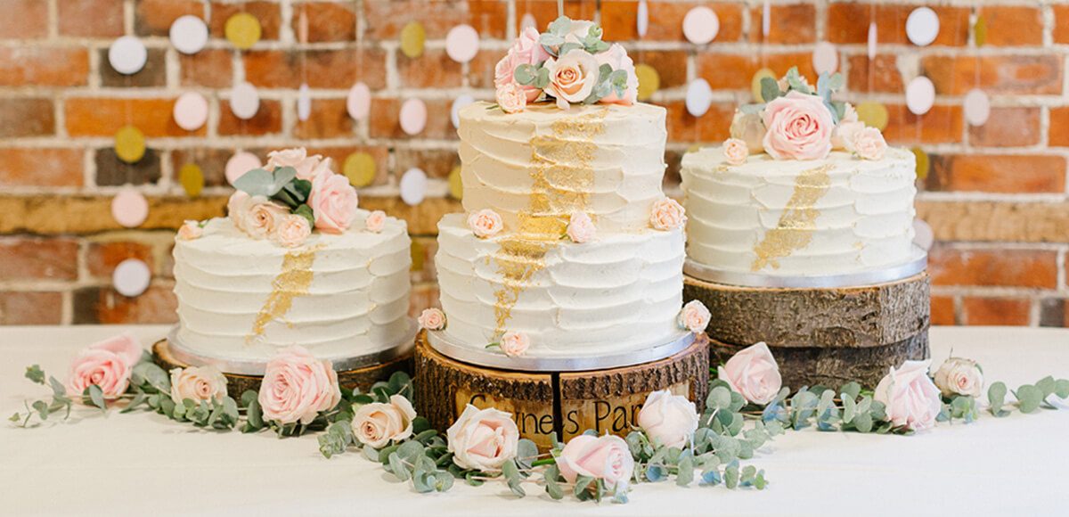 Three rustic wedding cakes wait to be cut during an evening wedding reception at Gaynes Park