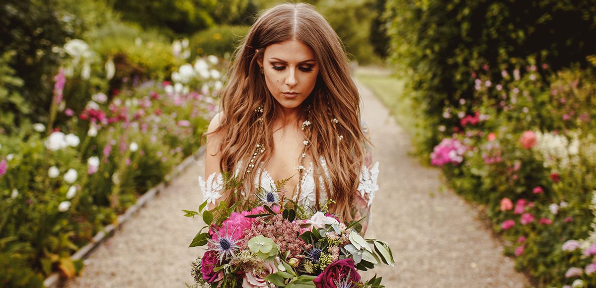 The boho bride holds a stunning wedding bouquet as she walks down the Long Walk to her wedding ceremony at Gaynes Park