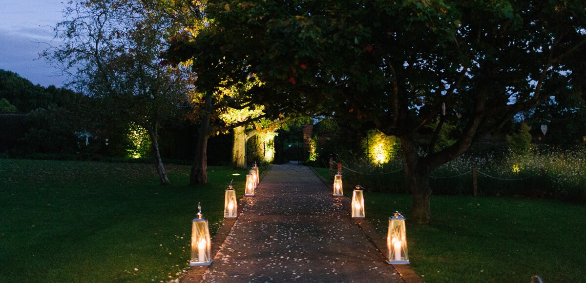 Lanterns light up the wedding aisle in the Walled Gardens during an evening reception at Gaynes Park in Essex
