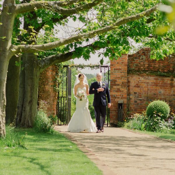 The bride to be walks down the wedding aisle in the Walled Garden at Gaynes Park on her summer wedding day