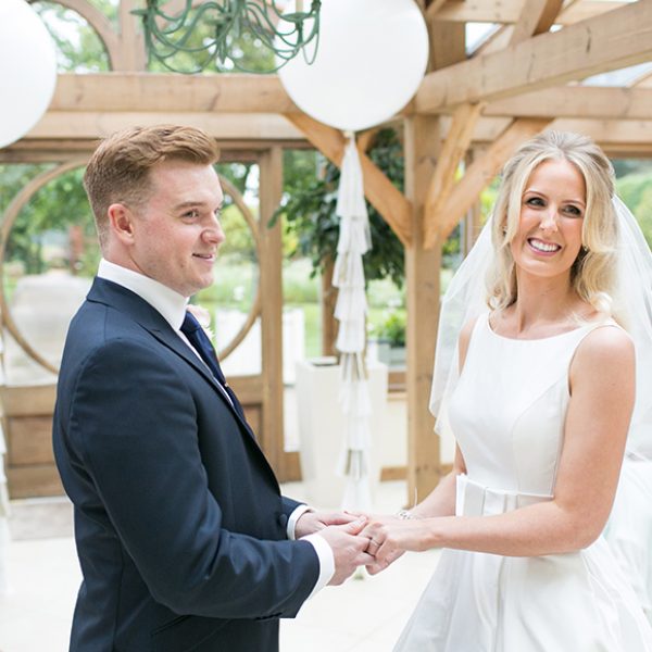 A couple say their wedding vows in the Orangery at Gaynes Park as white wedding balloons hang in the background